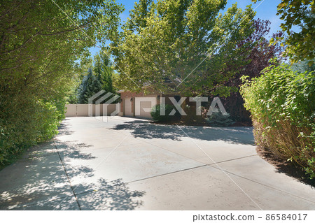 Large backyard of a house with concrete driveway in the middle of trees and plants 86584017