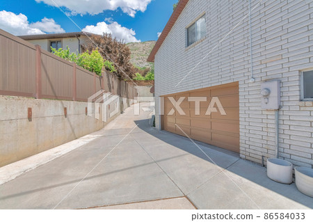 Uphill curved driveway beside the garage with sliding window and white texture bricks wall 86584033
