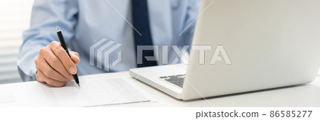 Working Man Conept The male officer sitting in the office, laying his left hand on the laptop, and writing something on the paper with his right hand 86585277