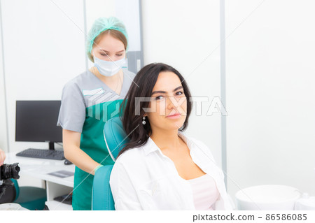 The dentist's assistant puts the protection on the patient, the napkin on the chest The dentist's assistant puts the protection on the patient, the napkin on the chest 86586085
