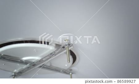 A close-up of the hands of an unrecognizable man inserting the base for mounting a ceiling light. Repair A close-up of the hands of an unrecognizable man inserting the base for mounting a ceiling light. Repair 86589927