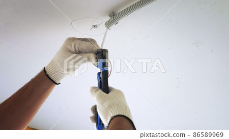 A male electrician connecting a ceiling lamp to electrical wires in a new apartment building. Close-up 86589969