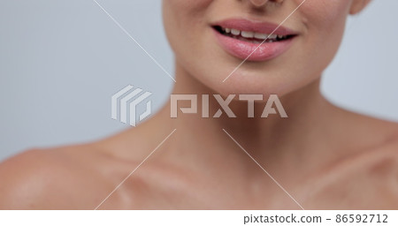 Close-up portrait of young woman with smooth healthy skin, gently touches her shoulders and face with her fingers on gray background and smiles. Skincare concept. 86592712