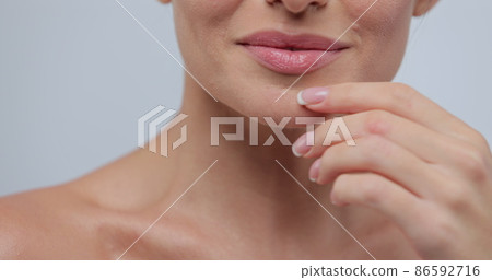 Close-up portrait of young woman with smooth healthy skin, gently touches her shoulders and face with her fingers on gray background and smiles. Skincare concept. 86592716
