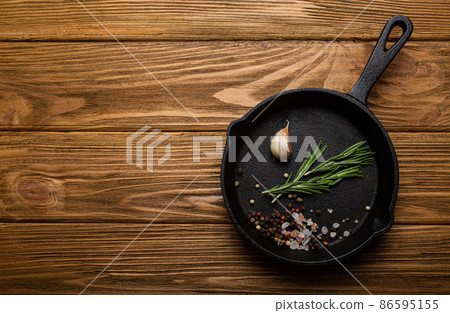 Black cast iron frying pan skillet with food cooking ingredients fresh rosemary, garlic, salt and pepper Black cast iron frying pan skillet with food cooking ingredients fresh rosemary, garlic, salt and pepper 86595155