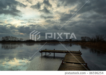 A pier on a frozen lake and dark clouds 86596254
