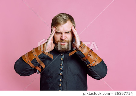 Portrait of young bearded man in image of medieval warrior, archer suffering from pain, touching temples in headache isolated over pink background 86597734
