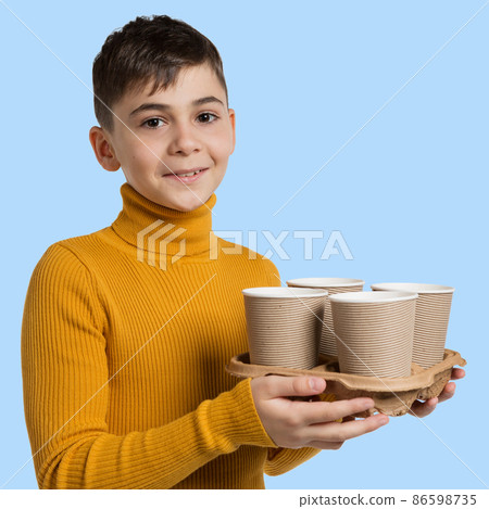 a boy, smiling, holds a tray with four cardboard glasses of tea or coffee in his hands, concept 86598735