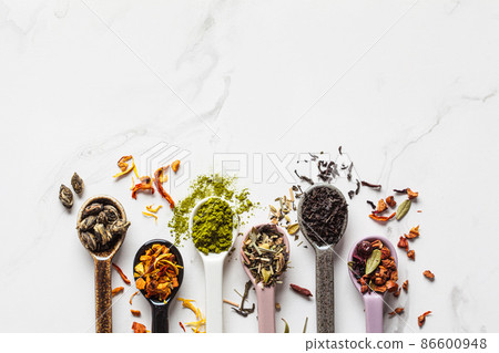 Various types of dry tea in spoons on white marble background. Green tea, matcha, citrus tea, black tea and herbal detox tea. 86600948