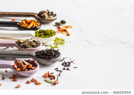 Various types of dry tea in spoons on white marble background. Green tea, matcha, citrus tea, black tea and herbal detox tea. 86600949
