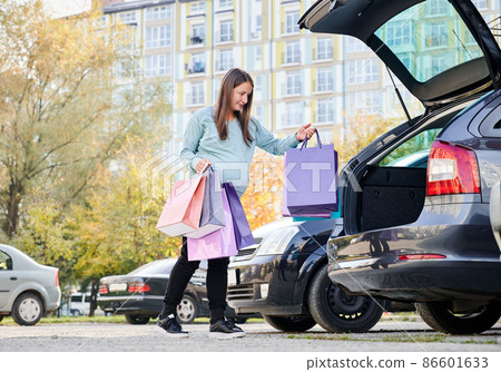 Woman with belly puting shopping bags in vehicle trunk, enjoying maternity and parenthood in awaiting mode. Pregnant female with purchase preparing for baby birth during weekend in city. Woman with belly puting shopping bags in vehicle trunk, enjoying maternity and parenthood in awaiting mode. Pregnant female with purchase preparing for baby birth during weekend in city. 86601633