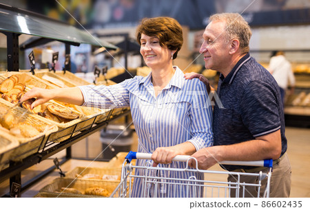 Elderly couple buys bread and baking in grocery section of supermarket Elderly couple buys bread and baking in grocery section of supermarket 86602435