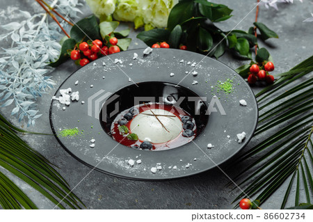 Panna cotta with raspberry sauce in a black plate 86602734