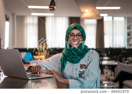 Business woman wearing a green hijab using laptop in relaxation area at modern open plan startup office. Selective focus  86602970