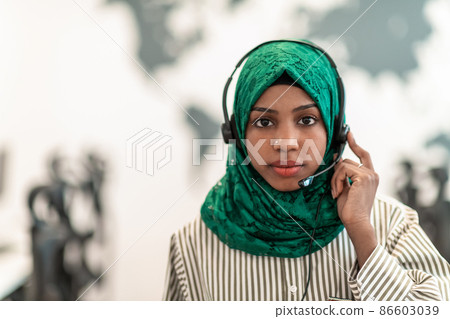 Afro Muslim female with green hijab scarf customer representative business woman with phone headset helping and supporting online with customer in modern call centre 86603039