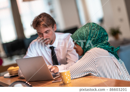 International multicultural business team.Man and muslim woman with hijab working together using smartphone and laptop coxation area at modern open plan startup officemputer in rela International multicultural business team.Man and muslim woman with hijab working together using smartphone and laptop coxation area at modern open plan startup officemputer in rela 86603201