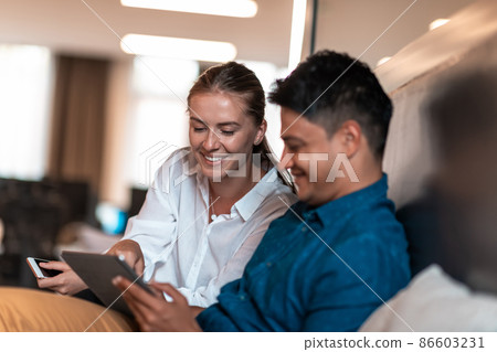 Multiethnic business people man with a female colleague working together on tablet computer in relaxation area of modern startup office Multiethnic business people man with a female colleague working together on tablet computer in relaxation area of modern startup office 86603231