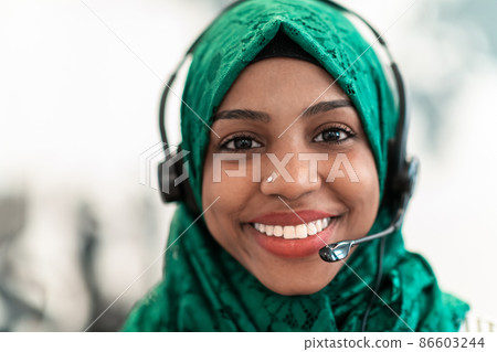Afro Muslim female with green hijab scarf customer representative business woman with phone headset helping and supporting online with customer in modern call centre Afro Muslim female with green hijab scarf customer representative business woman with phone headset helping and supporting online with customer in modern call centre 86603244