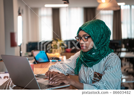 Business woman wearing a green hijab using laptop in relaxation area at modern open plan startup office. Selective focus  86603482