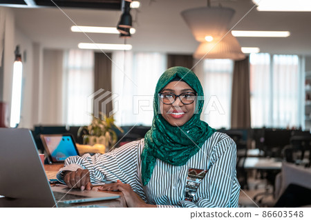 Business woman wearing a green hijab using laptop in relaxation area at modern open plan startup office. Selective focus Business woman wearing a green hijab using laptop in relaxation area at modern open plan startup office. Selective focus 86603548
