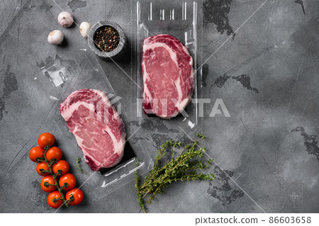 Rib-eye beef steak in plastic packing tray, on gray stone table background, top view flat lay, with copy space for text 86603658