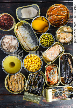 Canned preserves food in tin open cans. with fresh organic ingridients Saury, mackerel, sprats, sardines, pilchard, squid, tuna pinapple, corn, peas, mango , beans, over old wood dark textured 86603963