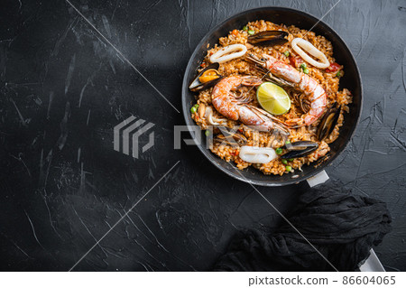 Traditional spanish seafood paella in pan rice, peas, shrimps, mussels and squid on black background, flat lay with copy space Traditional spanish seafood paella in pan rice, peas, shrimps, mussels and squid on black background, flat lay with copy space 86604065