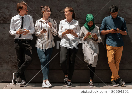 Multiethnic group of casual business people using mobile phone during coffee break from work in front of black wall outside 86604301