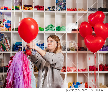 a woman inflates of helium from a red balloon. 86604376