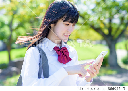 High school girl app SNS mobile phone smile that uses a smartphone in a beautiful fresh green park High school girl app SNS mobile phone smile that uses a smartphone in a beautiful fresh green park 86604545