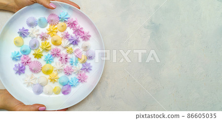 Top view of hands wich holds plate with delicious colorful meringue cookies . Sweet decor. Easter 86605035