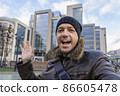 Cheerful man smiling and taking selfies while enjoying autumn day out in city. Successful man just got new business opportunity. Handsome caucasian man smiling happy taking selfie by camera walking at 86605478