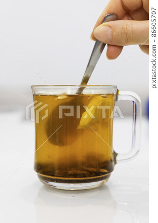 A glass cup of hot tea with honey and lemon on a light background. A glass cup of hot tea with honey and lemon on a light background. 86605707