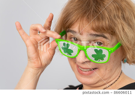 Portrait of a smiling elderly woman wearing clover-patterned glasses for st patrick's day Portrait of a smiling elderly woman wearing clover-patterned glasses for st patrick's day 86606011