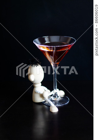 Toy wooden man hugging a martini glass on a black background. The concept of drunkenness, alcoholism. vertical photo 86606019