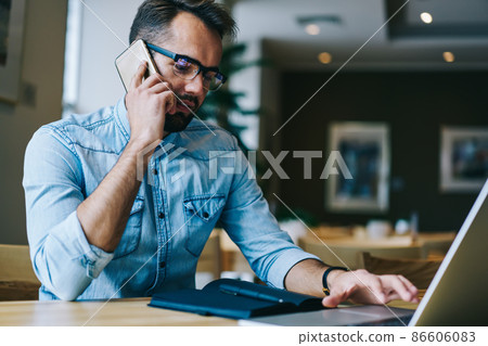 Focused man talking on phone working in cafe Focused man talking on phone working in cafe 86606083