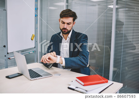 Serious businessman looking at wristwatch while working in office 86607593