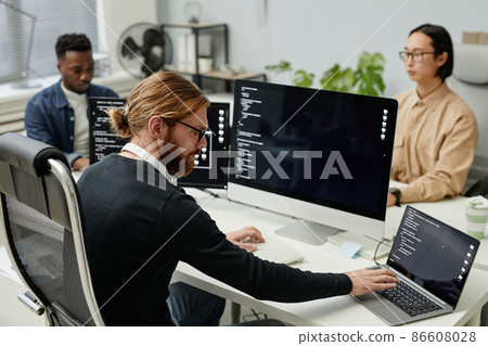 Young serious diversity programmer typing on laptop keyboard by workplace 86608028