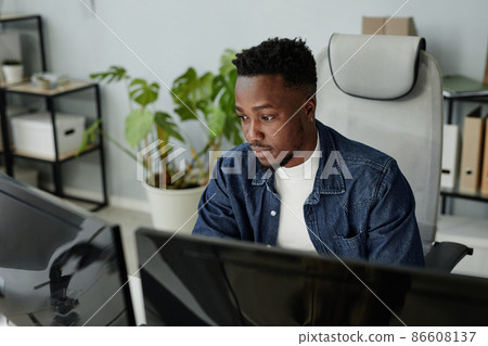Young blackman in casual clothes sitting in front of computer monitors 86608137