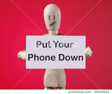 A wooden man holds a card with phrase Put Your Phone Down 86609082
