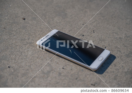 Phone with a broken screen on the pavement. Phone with a broken screen on the pavement. 86609634