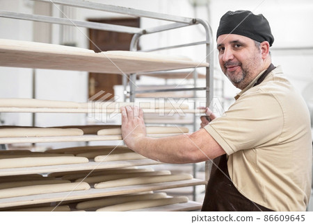 Confident baker posing with rack of fresh bread loaf at bakery. Confident baker posing with rack of fresh bread loaf at bakery. 86609645