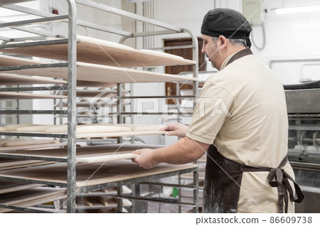 Baker working at industrial bakery preparing trays with fresh loaf. Baker working at industrial bakery preparing trays with fresh loaf. 86609738