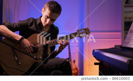 Man plays guitar. Young man plays a musical instrument. Musician records his composition in a music Studio using professional microphone 86610003