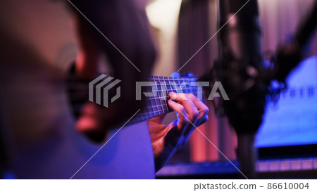 Close-up of the hands of a musician playing an acoustic guitar. Guitarist records music in the studio. Guitar and recording microphone close-up. 86610004