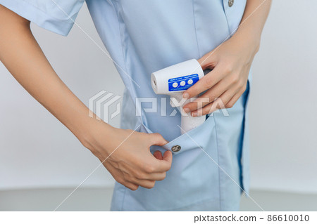 Temperature measurement gun in doctor hands. Close-up shot of doctor wearing protective surgical mask ready to use infrared isometric thermometer gun to check body temperature for virus symptoms. Temperature measurement gun in doctor hands. Close-up shot of doctor wearing protective surgical mask ready to use infrared isometric thermometer gun to check body temperature for virus symptoms. 86610010