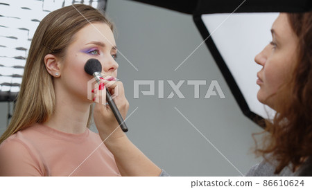A makeup artist makes up a model in the studio. 86610624
