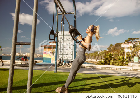 Fitness female training on suspension training equipment at park Fitness female training on suspension training equipment at park 86611489