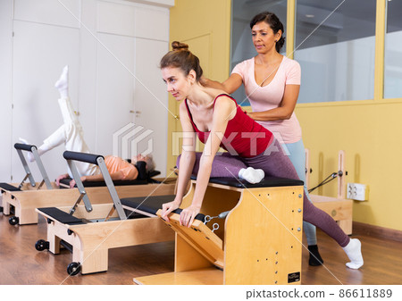 Young woman practicing pilates on wunda chair with Hispanic female trainer 86611889