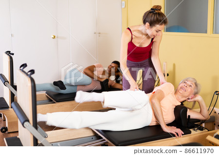 Senior woman exercising on pilates reformer with young trainer 86611970
